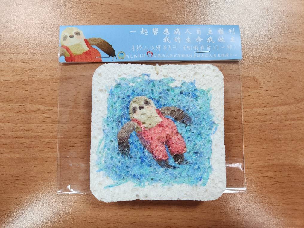 此款小物運用本中心出版之講述病人自主權利法重要性之繪本《樹懶爺爺的心願》，以書中代表角色樹懶爺爺為主角，製作木漿洗碗棉一款，希望藉由該項小物連結書中想傳達的意涵，讓民眾可以學習樹懶爺爺提早思考對於人生最後一哩路的醫療自主與安排。